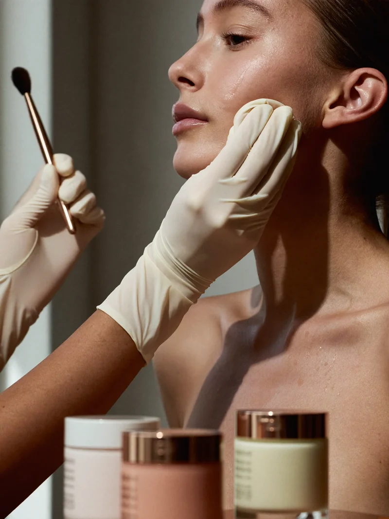 Hænder forbereder en models hud med svamp og pensel før makeup